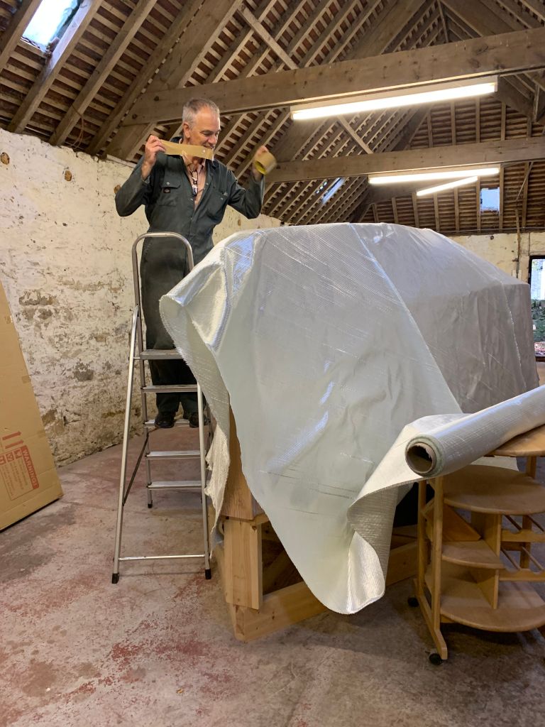 man standing on ladder next to building materials to construct a boat