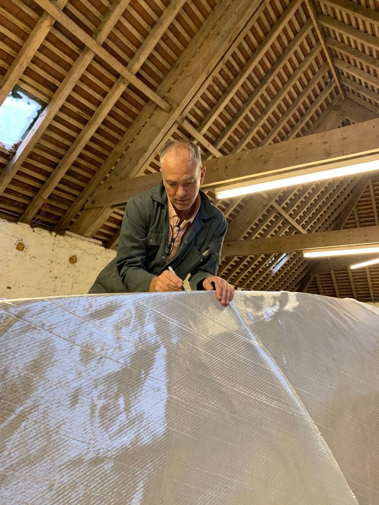 man measures material to build boat in wooden barn