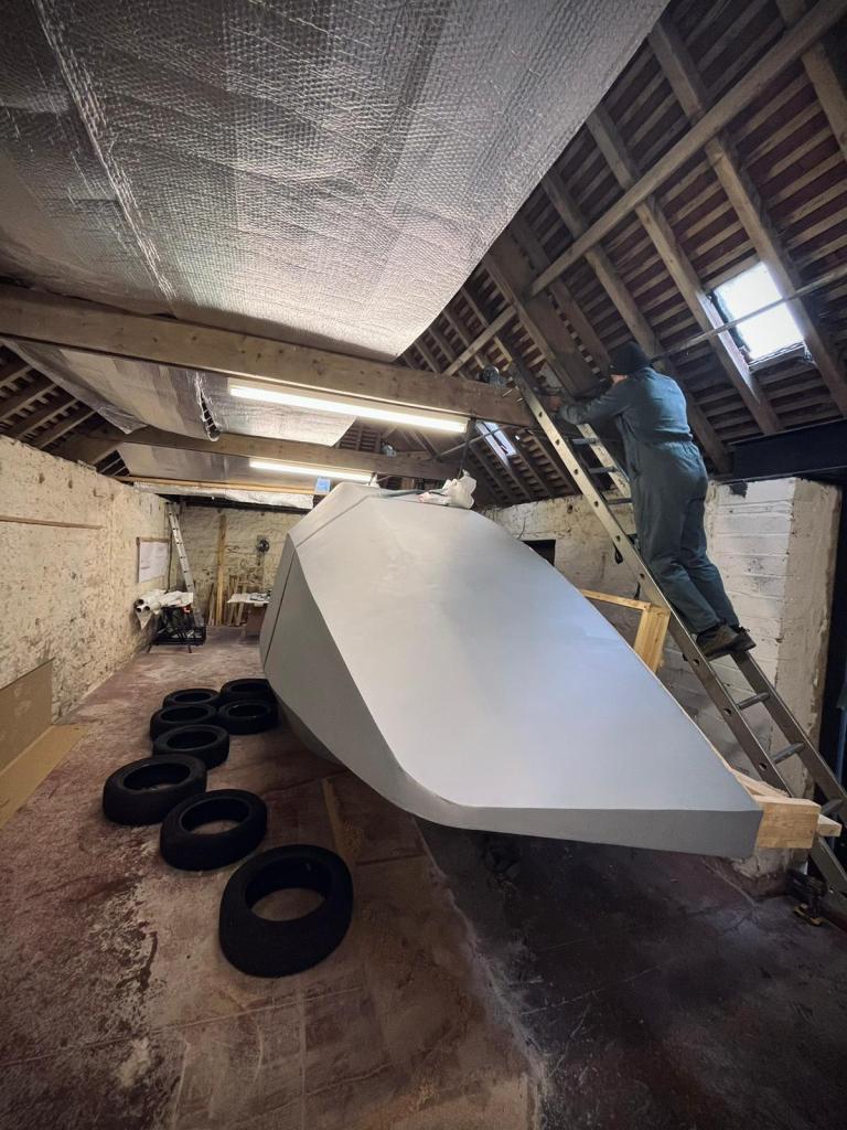 man in overalls and hat standing on a ladder looking over a boat turned on it's side