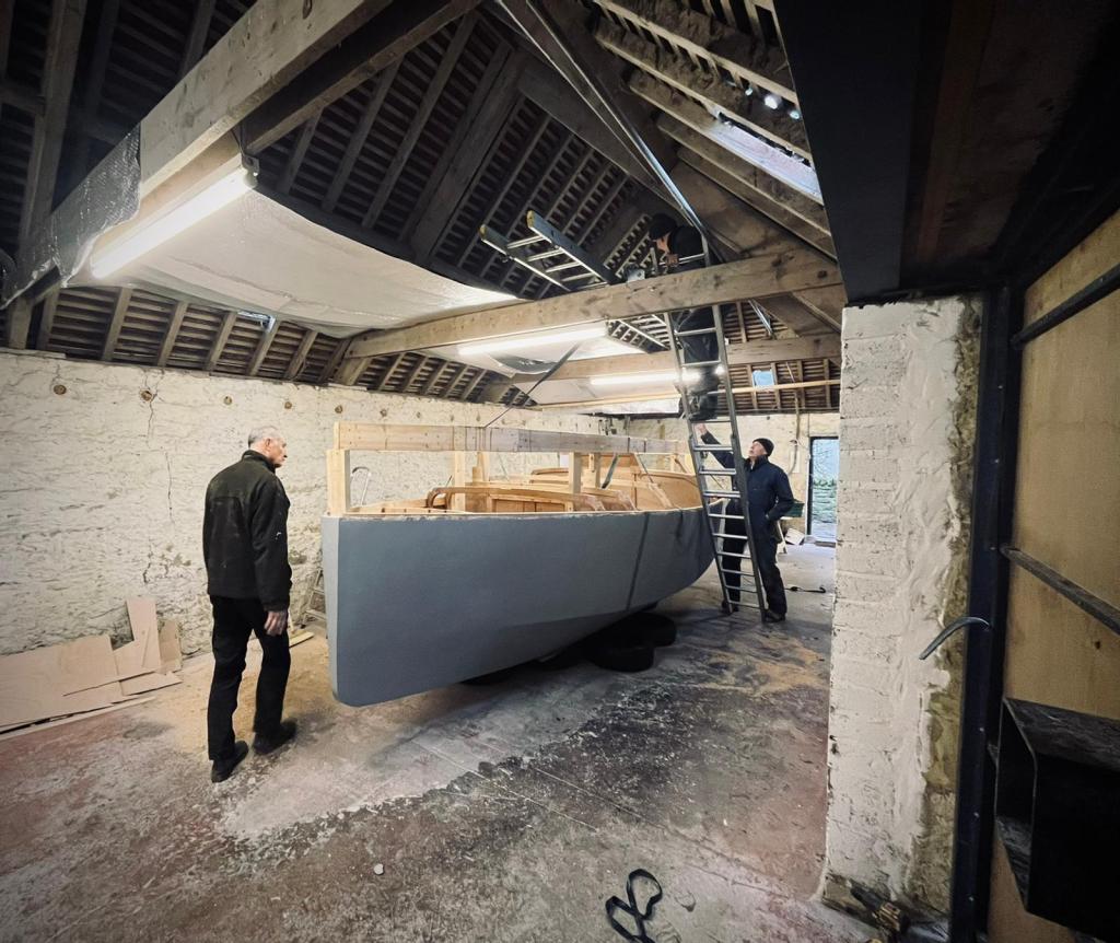 three men in a barn working on building an unfinished boat painted grey